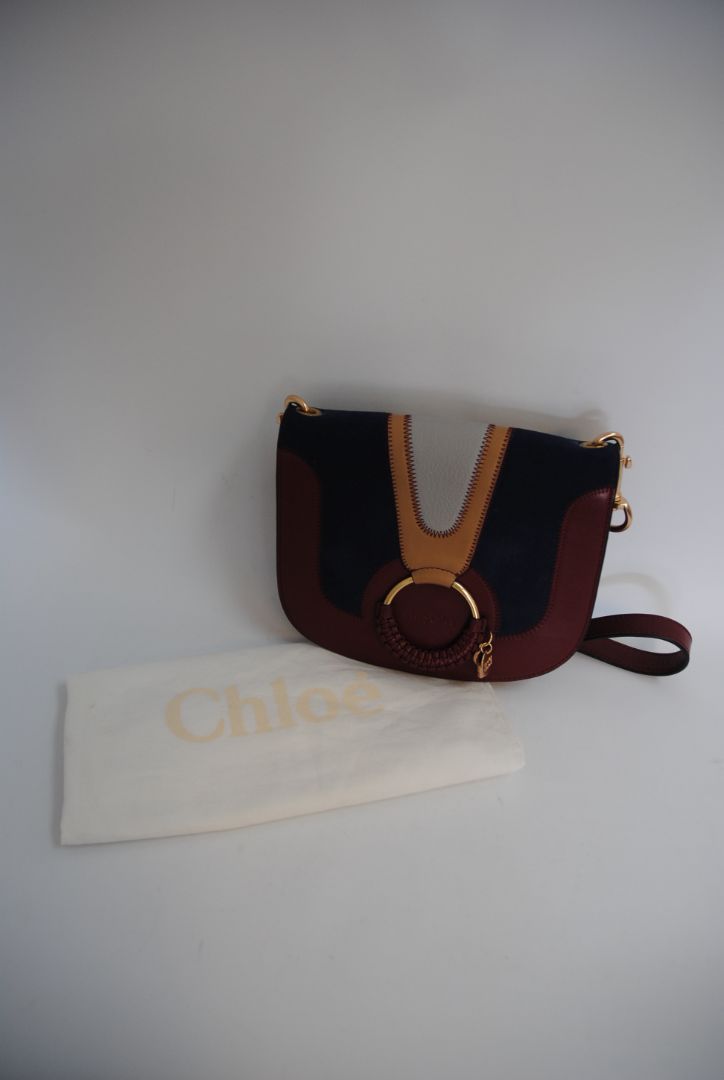 Body: Navy blue suede Trim & Strap: Burgundy and camel-toned smooth leather See by Chloe Hana Small Saddle Bag, Width: 7.5 in (19 cm) Height: 6.5 in (16.5 cm) Depth: 2.75 in (7 cm) Strap Drop: Adjustable up to approx. 22 in (crossbody length)