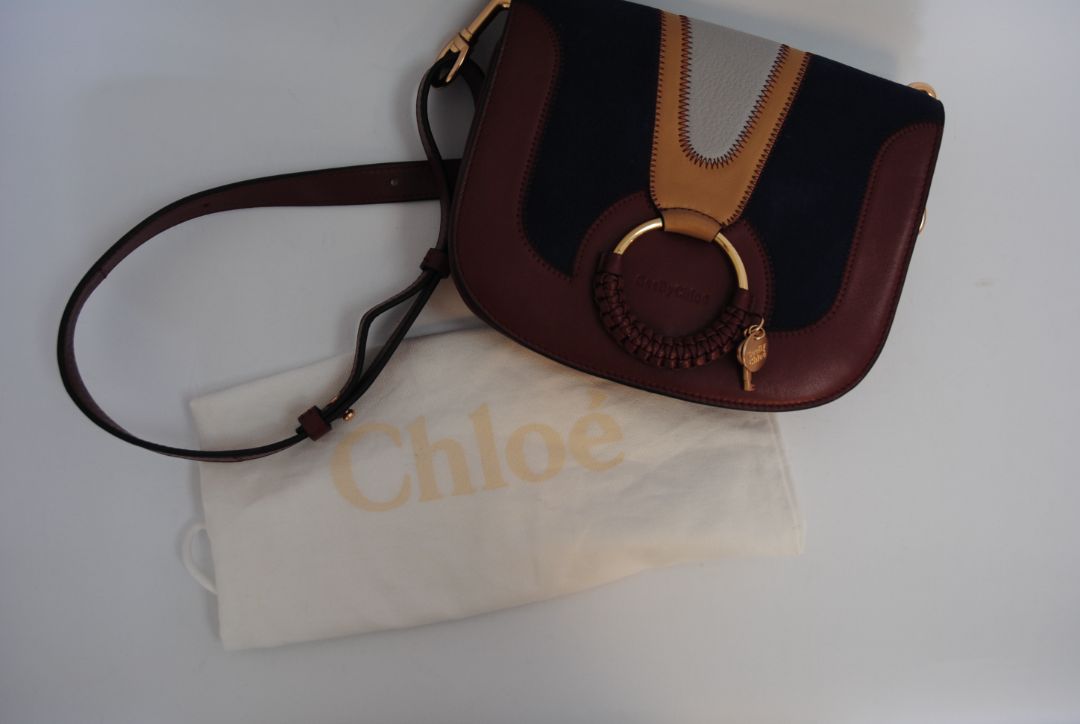 Body: Navy blue suede Trim & Strap: Burgundy and camel-toned smooth leather See by Chloe Hana Small Saddle Bag, Width: 7.5 in (19 cm) Height: 6.5 in (16.5 cm) Depth: 2.75 in (7 cm) Strap Drop: Adjustable up to approx. 22 in (crossbody length)