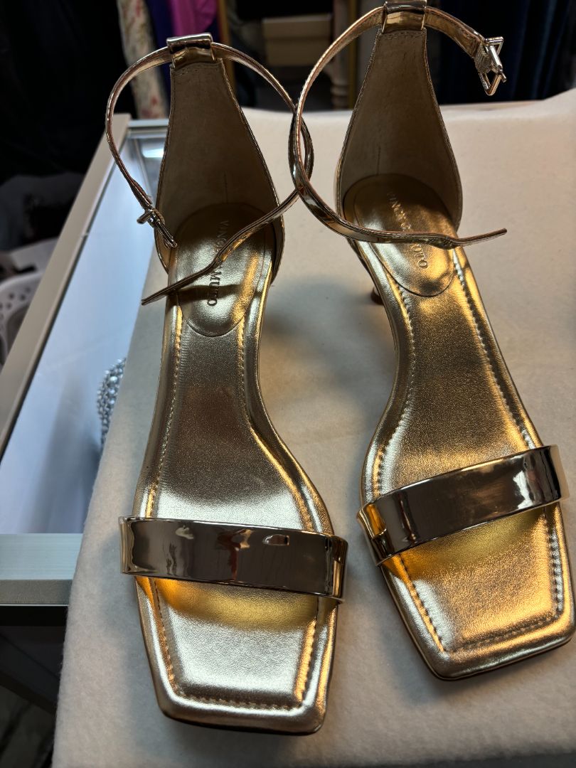 Vince Camuto gold strappy sandals with metallic finish, slim toe and ankle straps, and stiletto heel. New with tags, size 8M, displayed against a plain background.