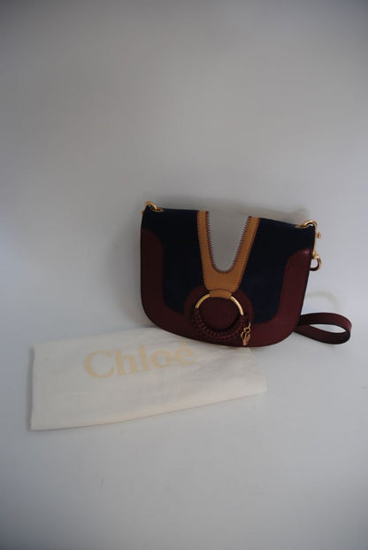 Body: Navy blue suede Trim & Strap: Burgundy and camel-toned smooth leather See by Chloe Hana Small Saddle Bag, Width: 7.5 in (19 cm) Height: 6.5 in (16.5 cm) Depth: 2.75 in (7 cm) Strap Drop: Adjustable up to approx. 22 in (crossbody length)