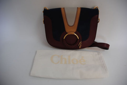 Body: Navy blue suede Trim & Strap: Burgundy and camel-toned smooth leather See by Chloe Hana Small Saddle Bag, Width: 7.5 in (19 cm) Height: 6.5 in (16.5 cm) Depth: 2.75 in (7 cm) Strap Drop: Adjustable up to approx. 22 in (crossbody length)