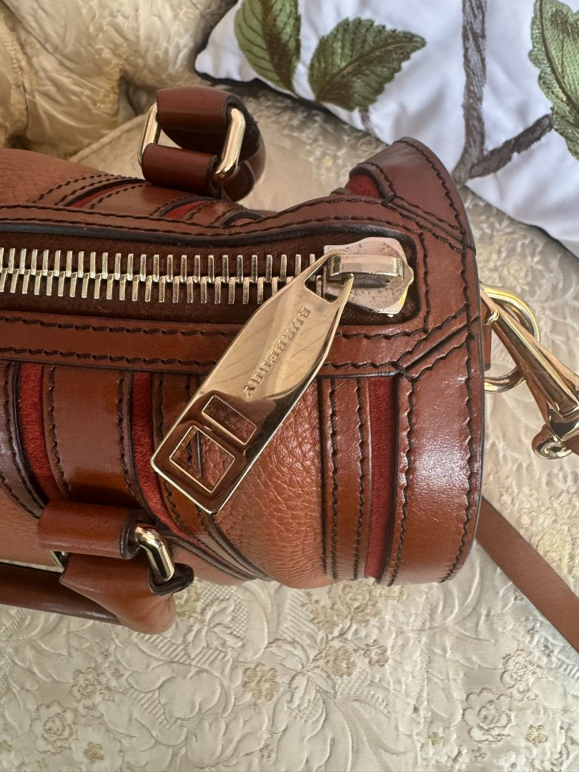 Cognac brown with multi-stripe accents in oxblood, black, and tan (subtle nod to Burberry’s house check palette) Burberry Model: Likely from the Banner or Orchard satchel line (structured silhouette with rolled handles and stripe accents), Length: 13 in (